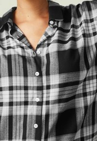 Chemise à carreaux noir et blanc avec un col, présentant une texture douce et des boutons blancs le long de la patte de boutonnage.