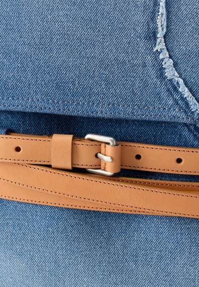 Ζώνη από ανοιχτό καφέ δέρμα με ασημένια αγκράφα σε μπλε τζιν με λεπτομέρεια ξεφτισμένης ραφής.