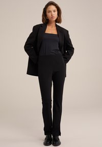 Černý přizpůsobený blejzr v kombinaci s těsným černým topem a černými kalhotami s vysokým pasem. Tento outfit má elegantní linie a hladkou texturu.