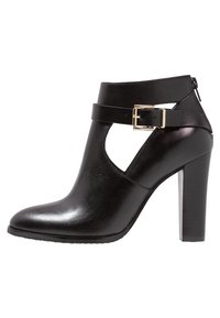 Musta nahkasaapas nilkkamittaisella varrella ja korkealla korolla, jossa on leikattu muotoilu ja solkivarustus. Silkkisen pehmeä pinta ja pyöreä kärki.