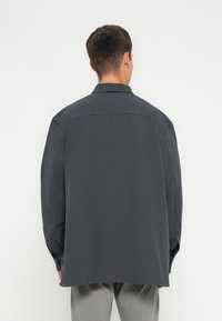 Dunkelgraues, oversized Hemd mit weicher Textur, langen Ärmeln, Knopfmanschetten und klassischem Kragen. Hervorstehende Nahtdetails.