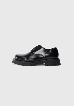 Schwarze, glänzende Lederschuhe mit Schnürung, ausgestattet mit einer dicken schwarzen Gummisohle und einem ausgeprägtenProfilmuster. Klassisches Design mit genähten Details.