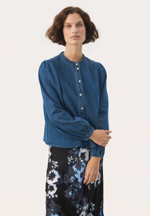 Denim gombos ing kerek nyakkal, puffos hosszú ujjal és laza fazonnal. Fekete virágmintás szoknya fölött viselve.