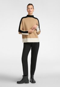 Maglione a blocchi di colore marrone, nero e bianco con collo alto, abbinato a pantaloni neri slim-fit e stivaletti neri. Texture morbida e vestibilità rilassata.