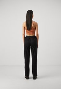 Strappy orange top with wave pattern paired with black, elastic-waist pants. Smooth texture, loose fit, full-length legs, and chunky shoes.