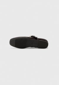Chaussure noire avec un upper en cuir lisse, des accents perforés et une fermeture à boucle. Semelle en caoutchouc avec des rainures horizontales pour une meilleure adhérence.