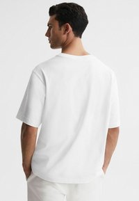 T-shirt bianca in cotone con maniche corte, scollo tondo e vestibilità rilassata, caratterizzata da una texture liscia e un design minimalista.