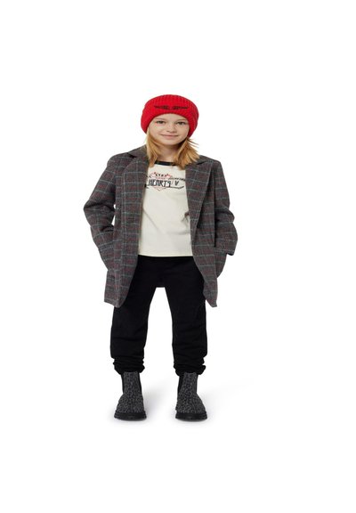 Geruite grijze jas met rode details, crèmekleurig shirt, zwarte broek en zwarte chelsea boots met een gestructureerd patroon; rode gebreide muts.