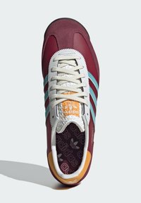 Červené a hnědočervené tenisky s tyrkysovými pruhy, bílými tkaničkami a oranžovým akcentem. Texturovaná špička a vzorovaná podšívka.