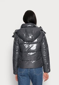 Błyszcząca szara kurtka puchowa z kapturem, z przeszytymi panelami i elastycznymi akcentami, w połączeniu z niebieskimi dżinsami.