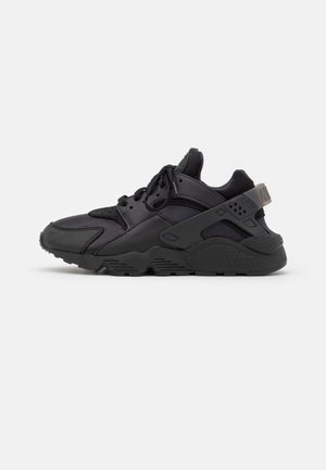 Baskets de sport noires avec des panneaux en mesh et en cuir, semelle épaisse, lacets et une sangle de maintien autour du talon, vues de côté.