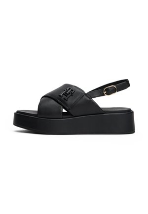 Black platform sandal with crisscross leather straps, gold buckle ankle strap, and embossed logo on upper strap.