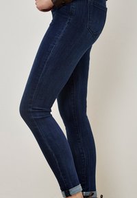 Jeans ajustados en denim azul oscuro, con una silueta ceñida, puños enrollados, detalles de costura y diseño tradicional de cinco bolsillos.
