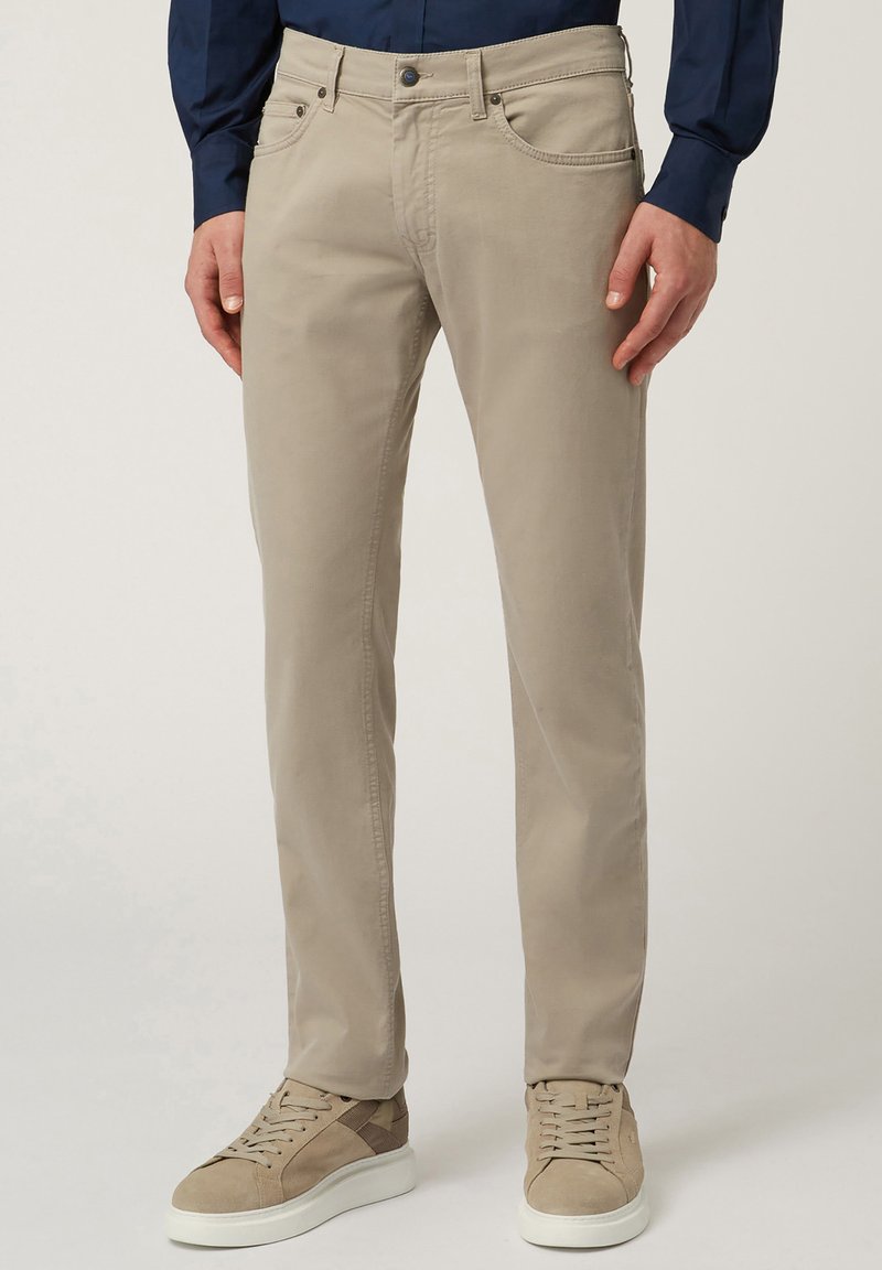 Beige katoenen chinos met een rechte snit, vijf zakkenontwerp en metalen knoopsluiting, gecombineerd met lichtgekleurde sneakers en een marineblauw shirt.