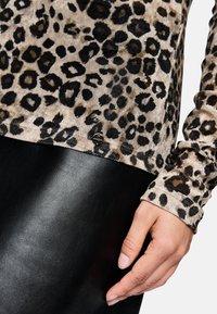 Top w leopardzi wzór w odcieniach brązu i czerni, wykonany z miękkiego materiału, z długimi rękawami, połączony z gładką, czarną skórzaną odzieżą.