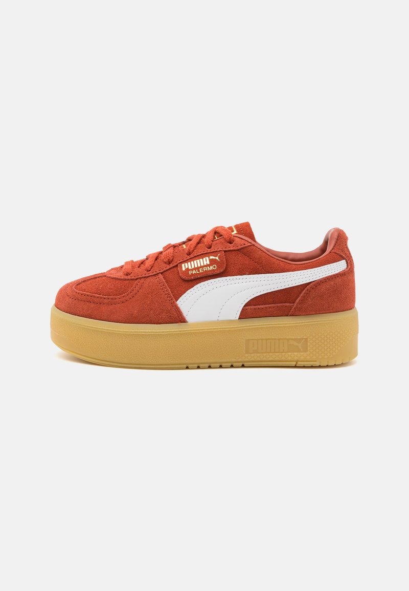 Red suede sneakers with a thick gum sole, featuring white accents and a logo tag on the side. Laced design with padded collar.