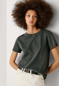 Tumedast hall puuvillane t-särk lühikeste varrukatega, ümar kaelus ja tekstuuriga graafiline disain esiküljel. Kantud musta nurgelise vöödiga.