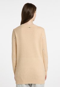 Beige gestrickter Pullover mit geripptem Rundhalsausschnitt, langen Ärmeln mit floralen Ausschnitten und lockerer Passform, die unter die Hüften reicht.