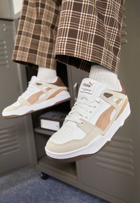 Baskets blanches et beiges avec des accents en daim et en mesh, dotées d'une semelle texturée, d'un marquage discret et d'un design sportif.