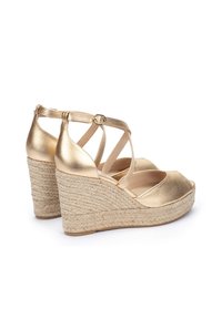 Sandalias de cuña metálicas doradas con una plantilla de yute trenzado, presentan un diseño de tiras cruzadas y cierre de hebilla en el tobillo.