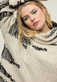 Übergroßer, gestrickter Pullover in Creme und Schwarz, mit einem strukturierten Muster, Cowl-Neck und lockeren Ärmeln. Gemütliches, warmes Material.