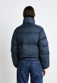 Mørkeblå dunjakke med høy krage og quiltet design; kombinert med denimjeans. Stoffet ser glatt og glansfullt ut.