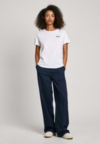 Camiseta blanca de algodón con mangas cortas y un pequeño logo. Pantalones de pierna ancha a rayas navy con bolsillos. Zapatillas blancas con acentos beige.