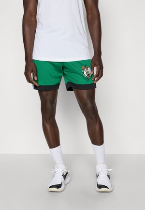 Green mesh basketball shorts with black trim, featuring a printed logo on the left leg. Worn with white socks and sneakers.