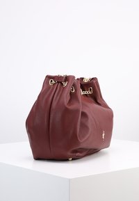 Bordowa skórzana torebka o teksturowanym wykończeniu, z marszczonym wykończeniem u góry, złotymi akcentami i detalem logo z boku.