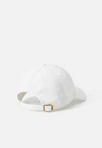Gorra de béisbol blanca vista desde atrás, con correa ajustable y hebilla de latón sobre un fondo blanco liso.