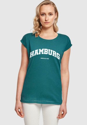 Tyrkysové tričko s krátkymi rukávmi s nápisom "HAMBURG" v bielom oblúkovom písme, vyrobené z jemnej bavlny. Dizajn zahŕňa okrúhly výstrih a voľný strih.