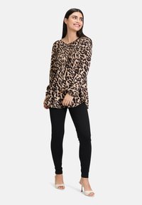 Haut à manches longues en imprimé léopard beige avec une coupe décontractée, associé à un leggings noir et des sandales à talons blocs blanches. Texture de tissu lisse.