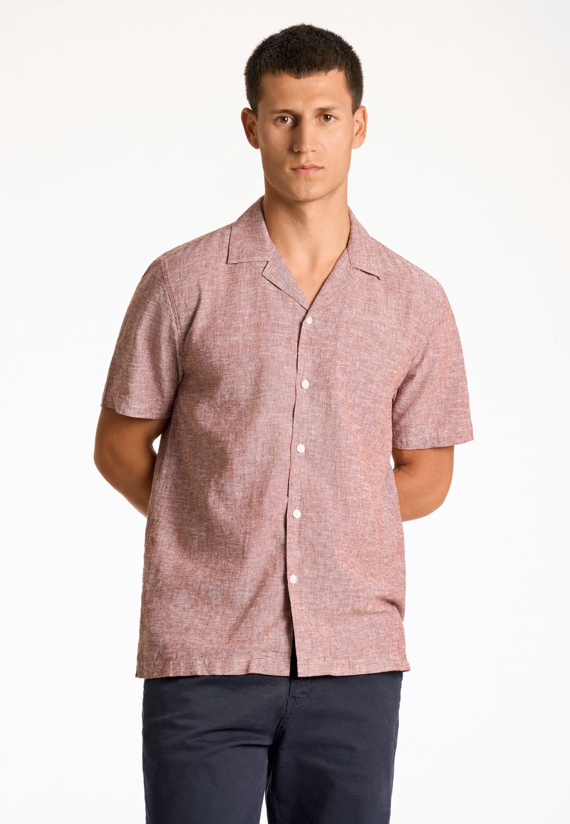 Camisa de manga corta, abotonada, en rojo claro con un patrón texturizado. Presenta un cuello con muesca y un corte relajado, combinada con pantalones oscuros.