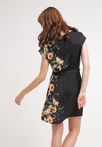 Vestido negro con mangas cortas, patrón floral en un lado, la tela parece suave con una cintura ajustada y un detalle de cinturón con lazo.