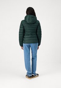 Zelená prošívaná bunda s vodorovnými prošívanými částmi, kapucí, doplněná světle modrými džíny a černými teniskami s bílými pruhy.