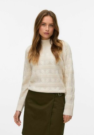 Sweter w kolorze kremowym, dziergany, z żebrowanym kołnierzem, charakteryzujący się teksturowanym wzorem i długimi rękawami, zestawiony z ciemnozieloną spódnicą z klamrą.