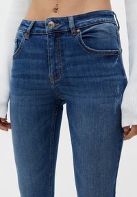 Jeans de denim azul ajustados con un lavado desvanecido, cinco bolsillos y costuras en contraste. Cuenta con un cierre de botón y una pretina de altura media.
