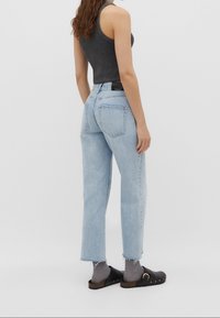 Jeans rectos de color azul claro con dobladillo deshilachado, diseño de cinco bolsillos y textura deslavada. Combinados con zuecos negros y calcetines gris oscuros.