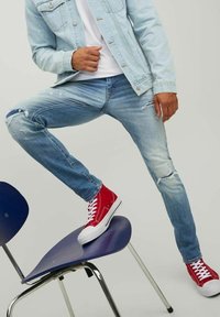 Ljusblå denimjeans med slitna detaljer, tillsammans med röda högsneakers. En ljusblå denimjacka fulländar den avslappnade stilen.