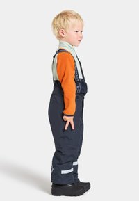 Marinblå overall med reflexstripes, ihop med en orange långärmad topp. Tillverkad av slitstarkt material; justerbara remmar synliga.