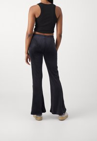 Black cropped tank top and dark flared pants made of soft fabric. Pants feature a smooth texture and slight sheen, with a comfortable fit.