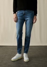 Blue denim jeans with a faded wash, straight-leg cut, and classic five-pocket design, paired with white sneakers.