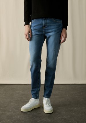 Blue denim jeans with a faded wash, straight-leg cut, and classic five-pocket design, paired with white sneakers.