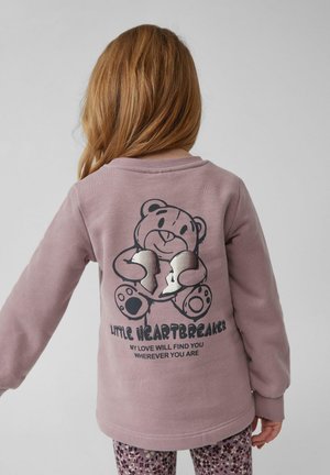 Jasnofioletowy sweatshirt z grafiką misia na plecach, zdobiony srebrnymi akcentami i tekstem. Długie rękawy oraz okrągły dekolt.