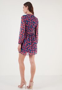 Langärmliges, blumig gemustertes Kleid in Lila, Pink und Grün mit einem elastischen Taillenbund, leicht durchscheinendem Stoff und rundem Ausschnitt.