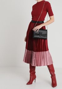 Haut côtelé rouge associé à une jupe midi plissée, passant d'un rouge foncé au rose. Sac à épaule noir et bottes rouges jusqu'aux genoux.