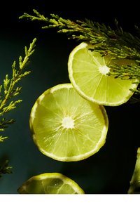 Pokrojona limonka z jasnobrązowym miąższem i jasnopomarańczową skórką, otoczona ciemnozielonymi liśćmi na czarnym tle.