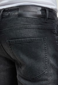 Mustat farkut matalla pinnalla, joissa on nahkainen etiketti nimeltä "ZY PREMIUM" ja hienovaraiset ompeluxksit takataskuissa.