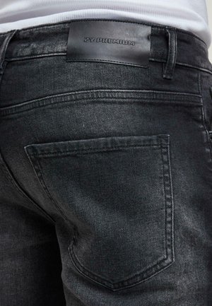 Zwarte spijkerbroek van denim met een matte afwerking, voorzien van een leren label met de tekst "ZY PREMIUM" en subtiele stiksels op de achterzakken.
