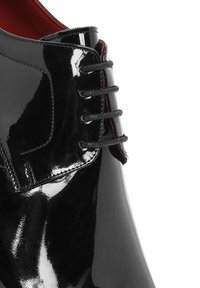 Glanzende zwarte leren schoen met zwarte veters en rode binnenvoering, close-up van het bovenwerk en vetersdetail.